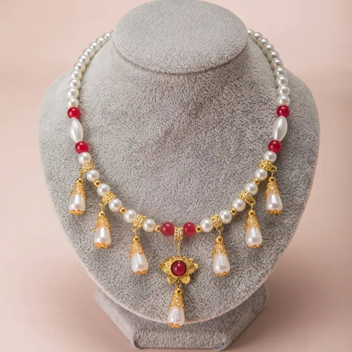 Luo Yue necklace with pearls, red beads and gold details, displayed on gray mannequin, close - up view