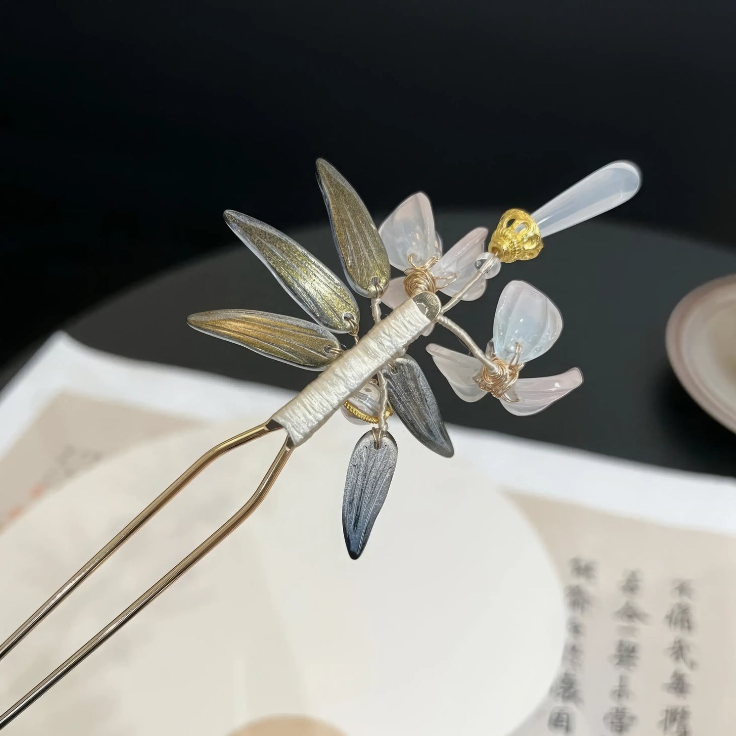 Closeup of the golden top piece on the magnolia hairpin, against a light wall with text paper