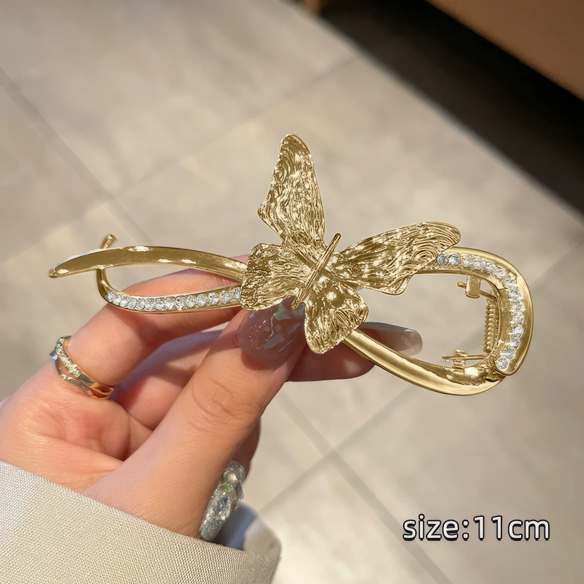 Hand holding gold metal butterfly twist clip, light surface background