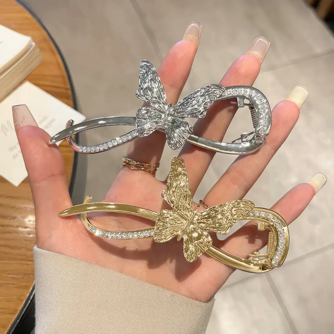 Hand holding mixed silver and gold metal butterfly twist clips, wooden table background