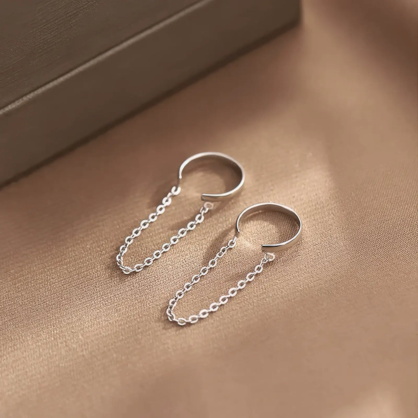 Pair of minimalist chain ear clips displayed on a brown surface, emphasizing the delicate chain and clip structure