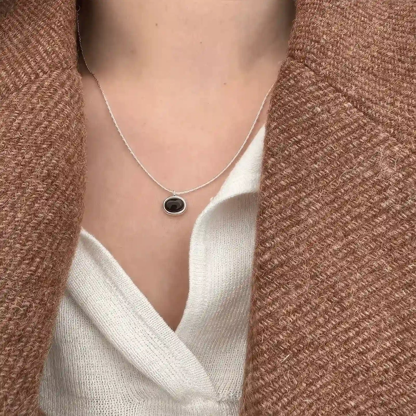 Oval black agate necklace worn, emphasizing the pendant against a white shirt and brown coat