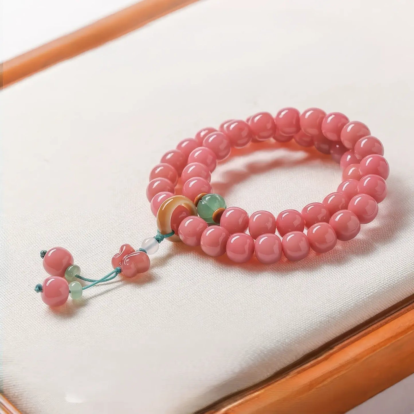 Single - strand peach pink white jade bodhi bracelet with beads and tassel, on white surface