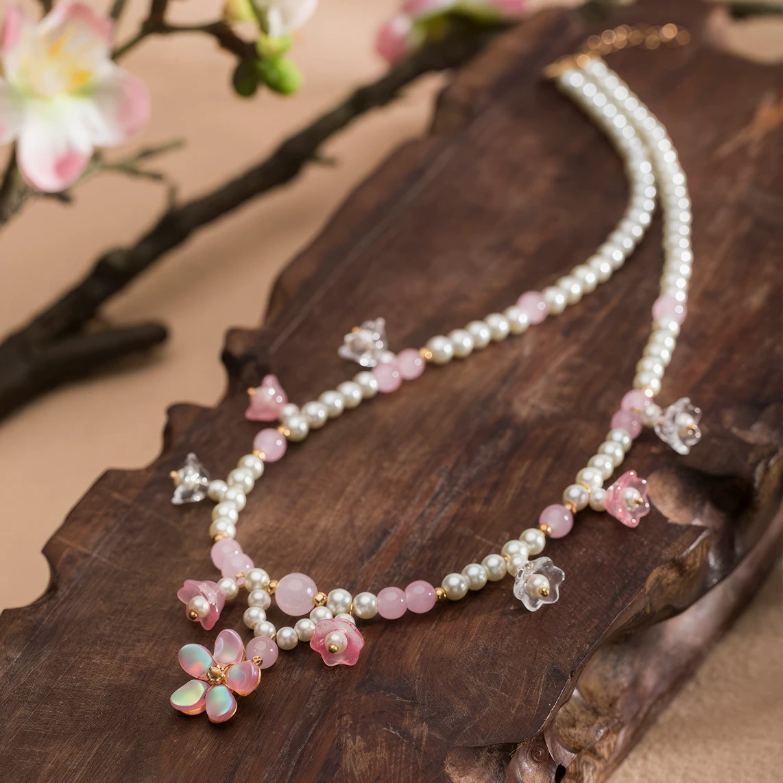Pink lily - of - valley necklace with pearls and pink beads, displayed on wooden board, flower in background