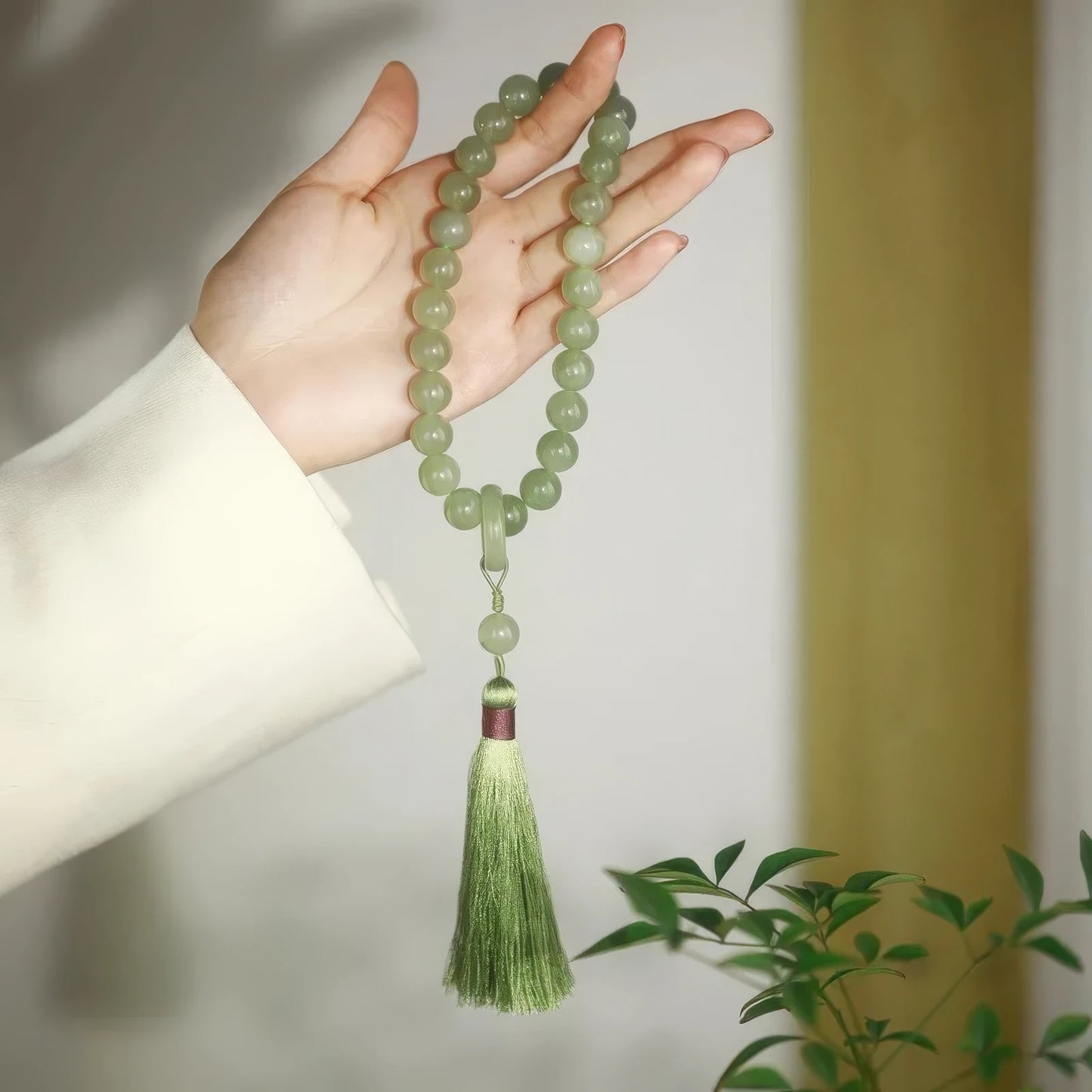 Hand holding Qingqingzijin bracelet as a long necklace, with greenery in background