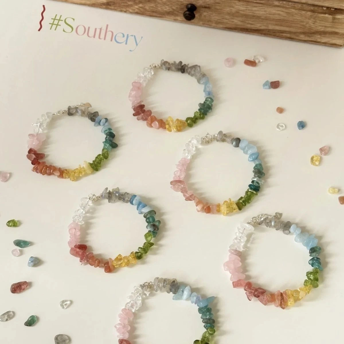 Multiple rainbow chip stone bracelets displayed with scattered stones on white surface