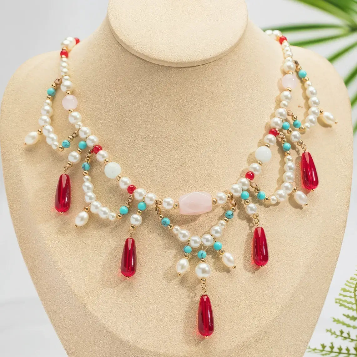 Red crystal water drop necklace with pearls and colorful beads, displayed on mannequin, light background