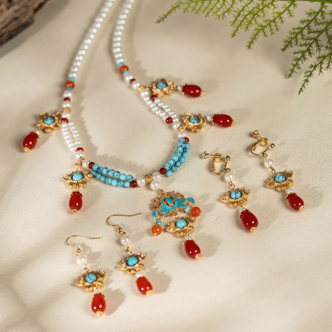 Red water drop lotus jewelry set (necklace and earrings) with pearls, turquoise and gold details, displayed on light fabric