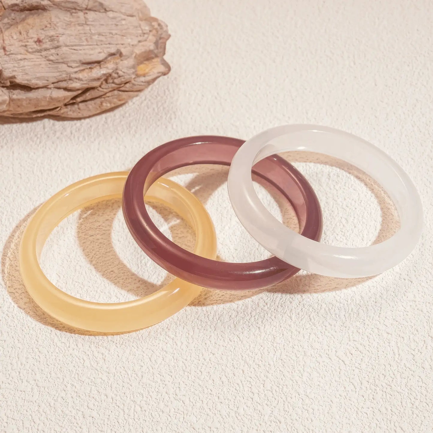 Yellow, purple, and white resin geometric round bangles placed on surface, showcasing collection