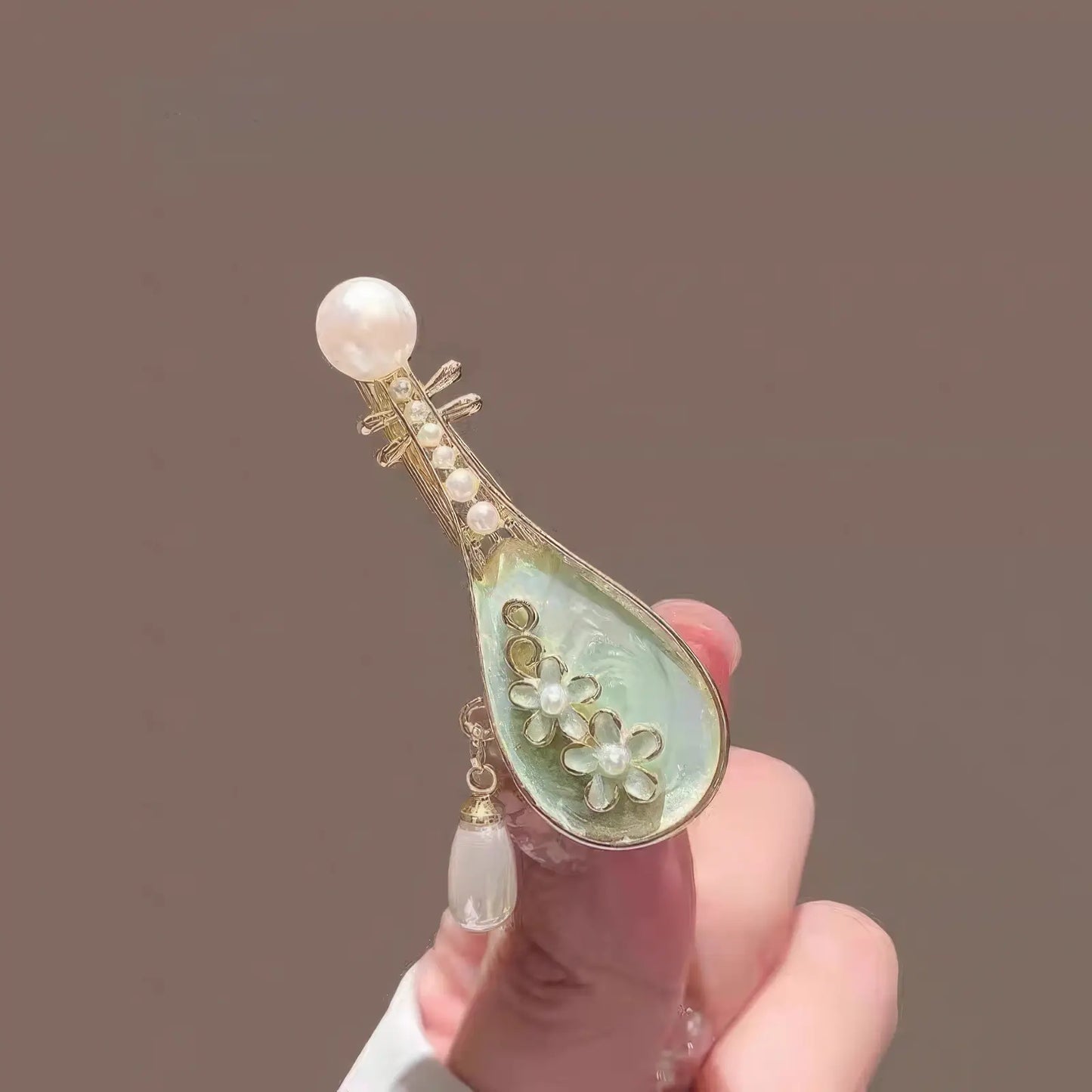 Hand holding rose pipa hair clip, close-up of floral details and pearl accents