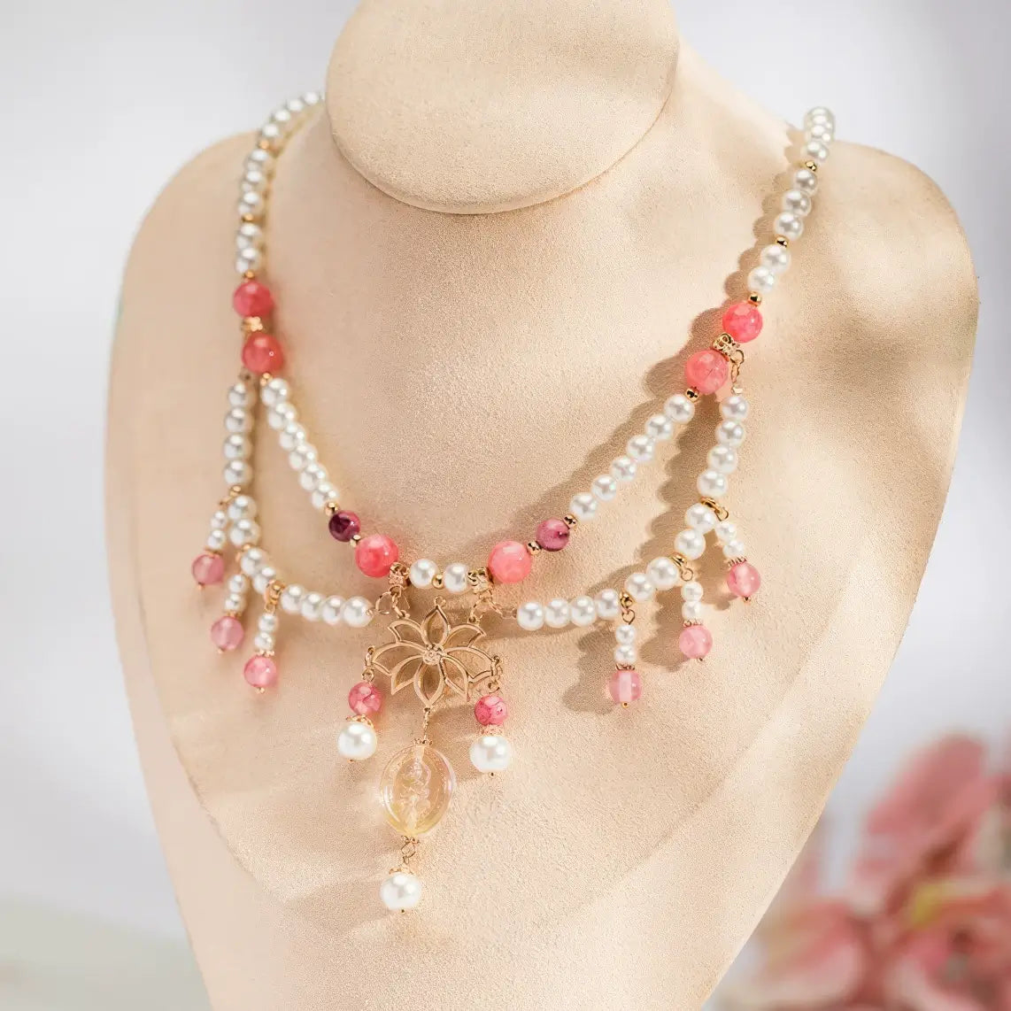Rose quartz lotus necklace with pearls, displayed on mannequin, light background