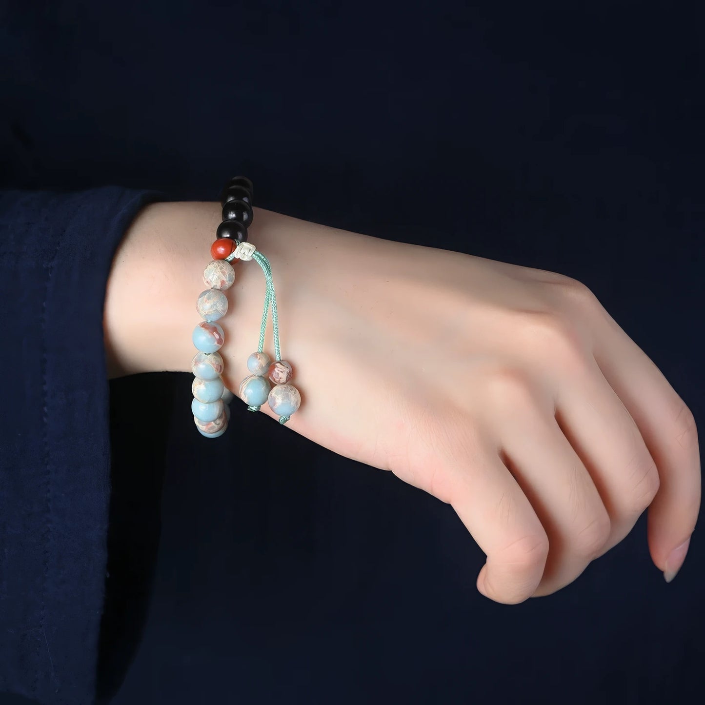 Multiple Shoushan stone and sandalwood bracelets worn on wrist, dark sleeve in background