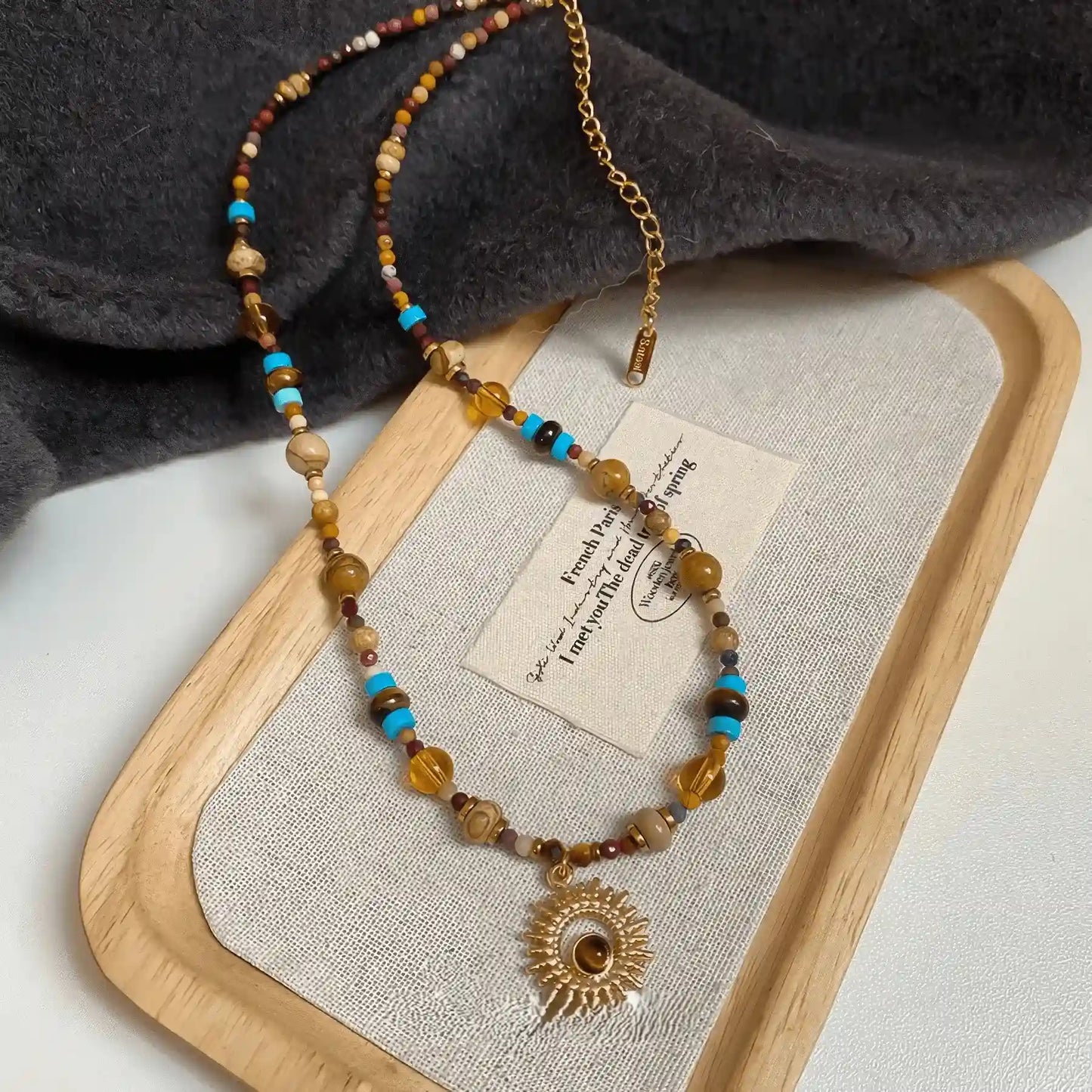 Sunflower beaded necklace, multi - color stones, gold - tone pendant, displayed on beige pad with wood trim