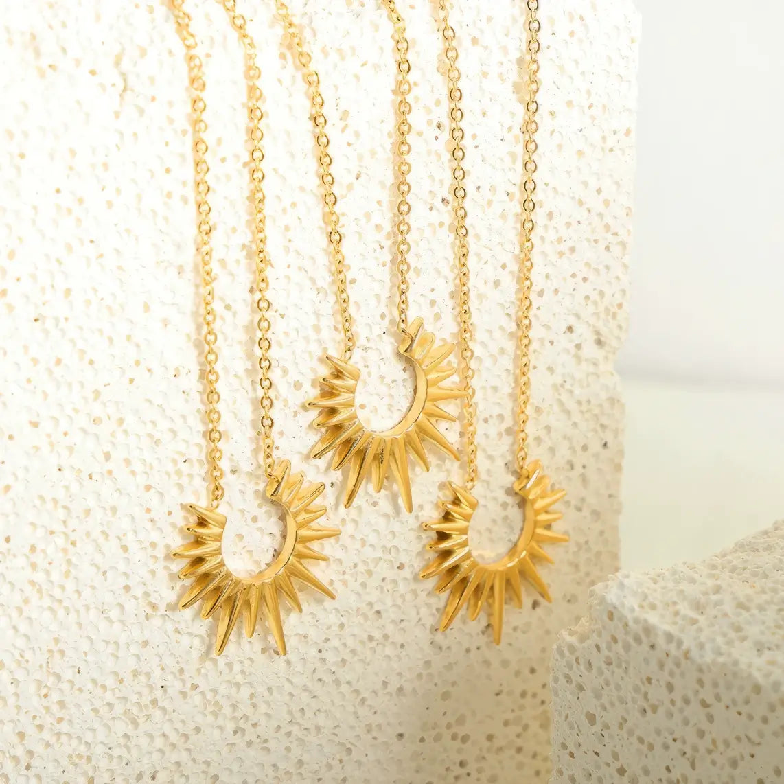 Multiple gold sunflower necklaces displayed on light surface