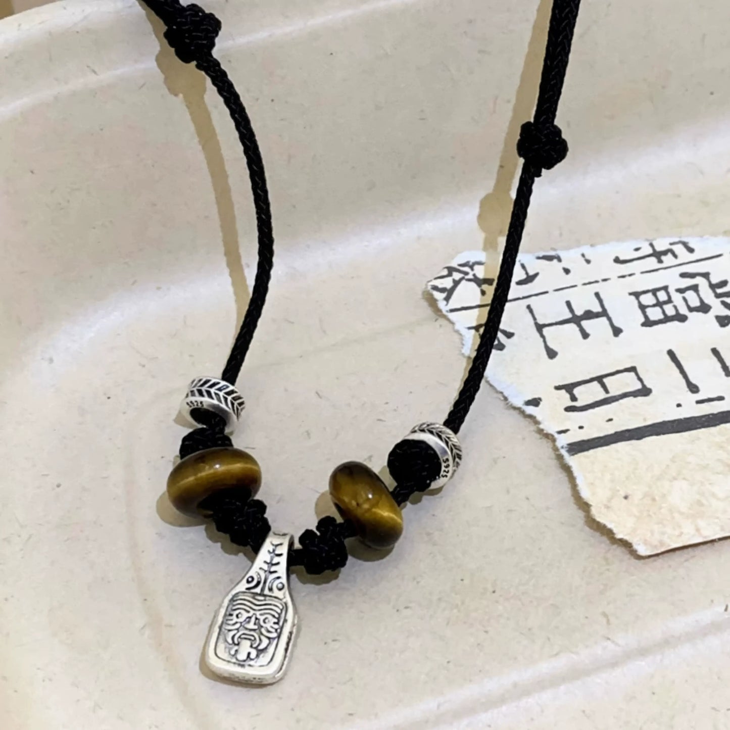 Tiger eye braided sliding knot pendant necklace displayed on a surface with paper, highlighting the details of the pendant and beads