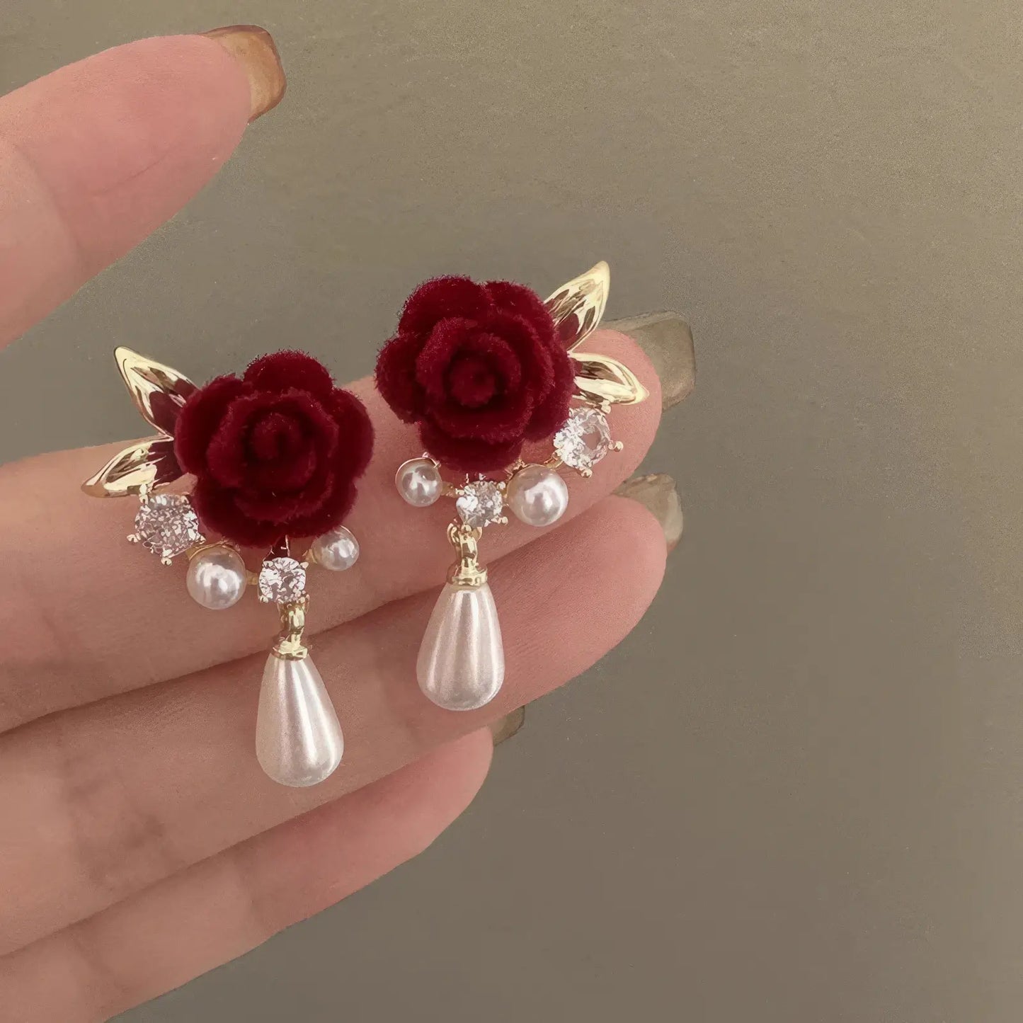 Red velvet rose earrings with crystals and pearl drops held by fingers