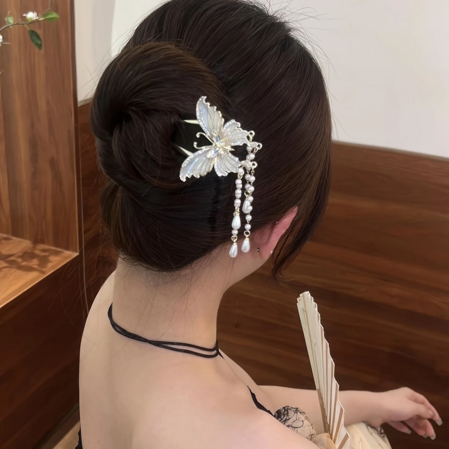White U - shaped butterfly hairpin worn in an updo hairstyle, traditional clothing background, holding a fan