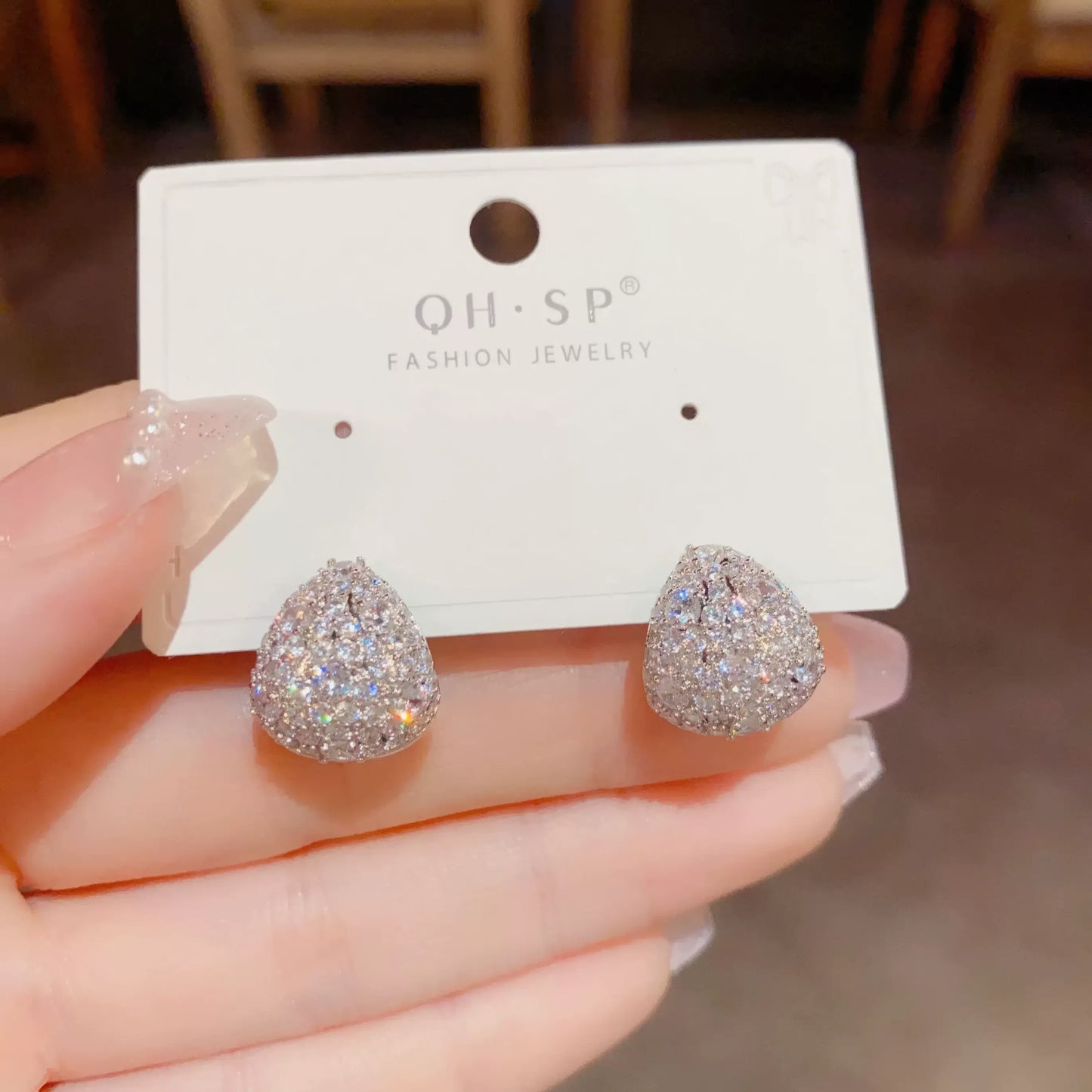 Silver zircon water - drop earrings on "QII·SP" card, held by hand, emphasizing sparkle