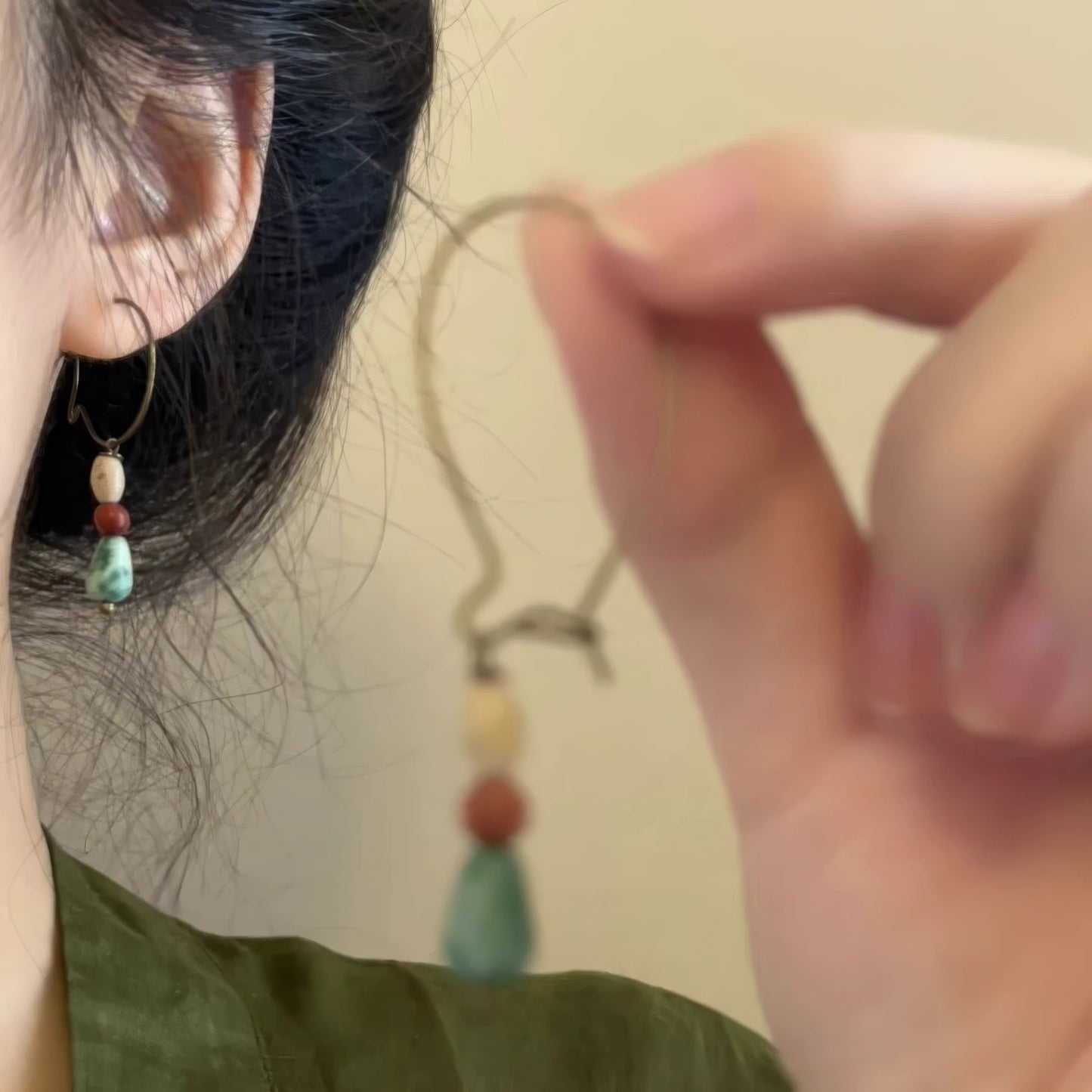  Hand holding an agate picture stone pendant earring, with one earring worn, showcasing the intricate bead and stone design.