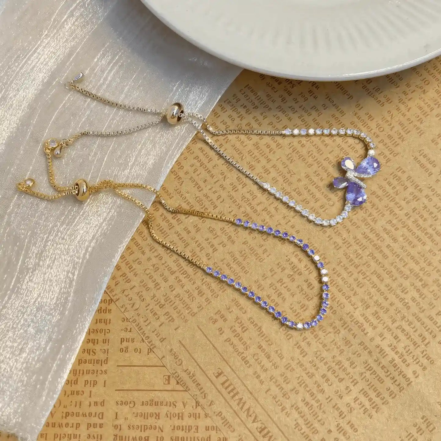 Set of amethyst butterfly bracelets placed on a textured surface with a plate.
