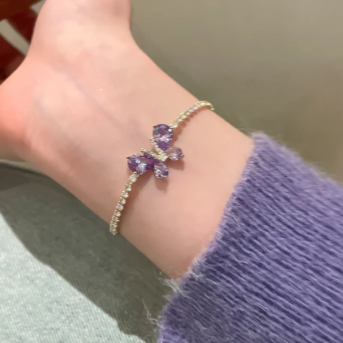 Single amethyst butterfly bracelet worn on wrist, with a purple sweater sleeve.