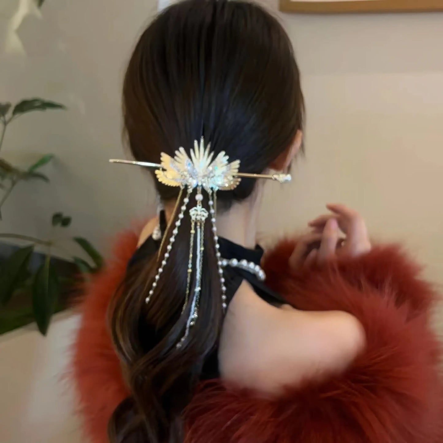 Elegant golden angel wing hairpin with dangling pearl tassels, worn to fix low half-up hair, matched with fluffy red fur outerwear for a luxurious retro look.