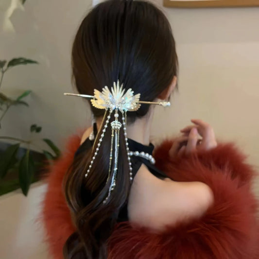 Elegant golden angel wing hairpin with dangling pearl tassels, worn to fix low half-up hair, matched with fluffy red fur outerwear for a luxurious retro look.