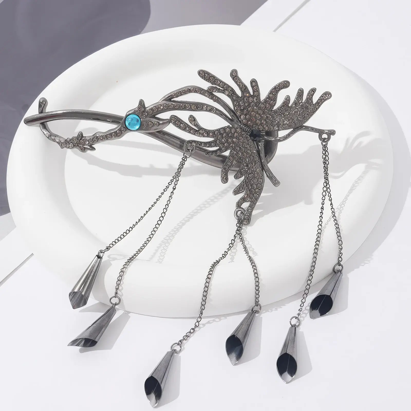 Black-toned butterfly twist clip laid flat on a white plate, showing the dark metal finish and bell-shaped tassels.