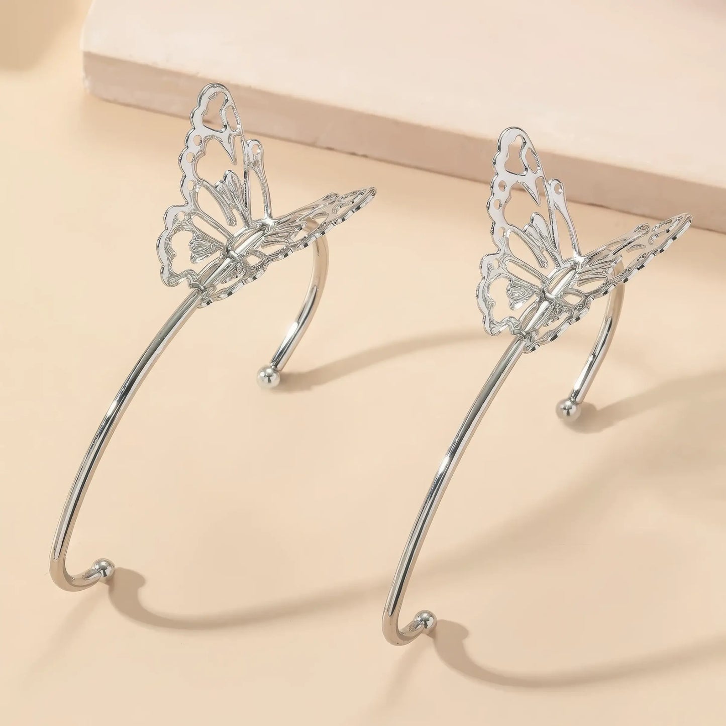  Pair of butterfly - style ear cuffs placed on a light - colored surface, showcasing detailed butterfly wings.