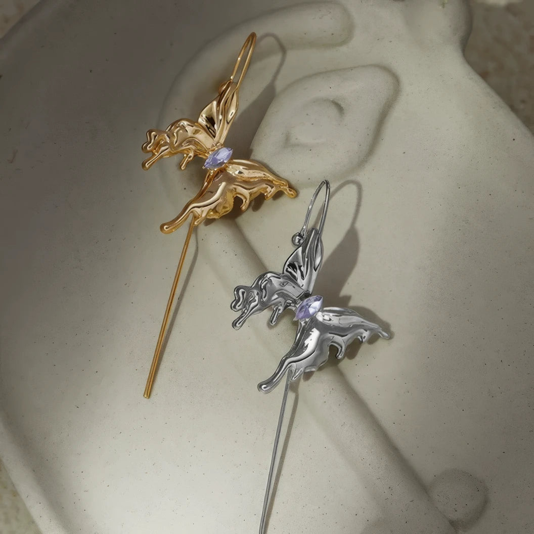 Pair of butterfly ear cuffs (gold and silver) placed on a light - colored surface.