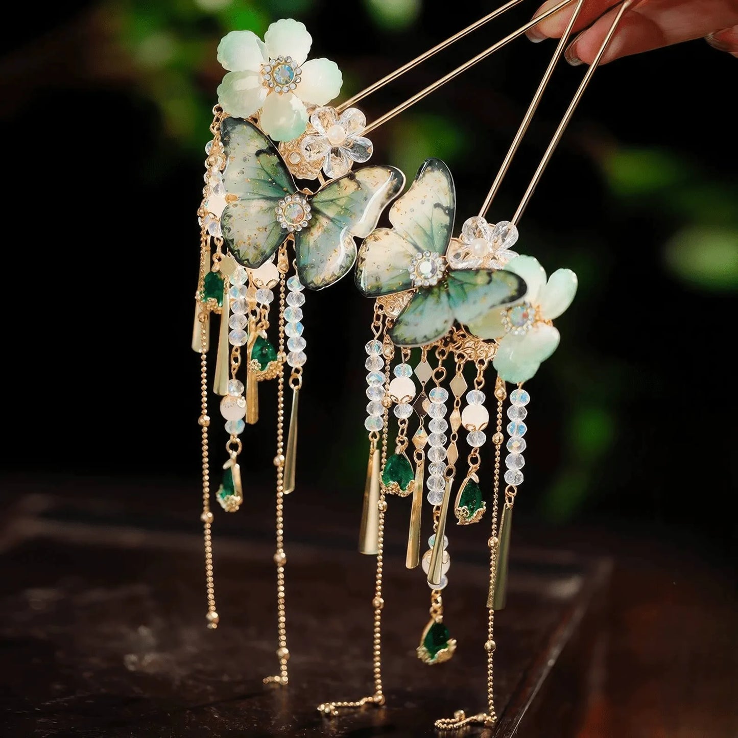 A pair of vintage hairpins decorated with white flowers and green butterfly ornaments, with long multi-layer crystal and metal tassels hanging down.