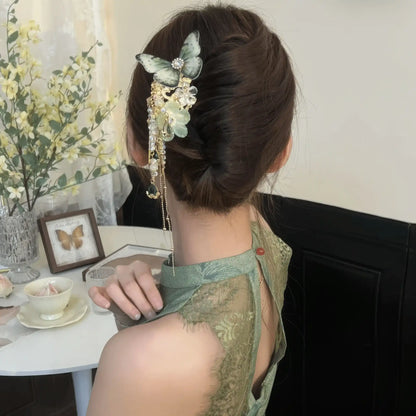 Green butterfly flower hairpin styled in low bun with green lace top, tassels resting near wearer’s shoulder.