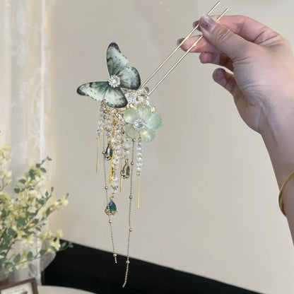 Single green translucent butterfly flower hairpin held by hand, multi-tier crystal tassels dangling below floral center.