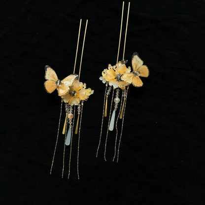 Close-up of paired yellow butterfly flower hairpins against black background, showcasing thin pins and short delicate tassels.
