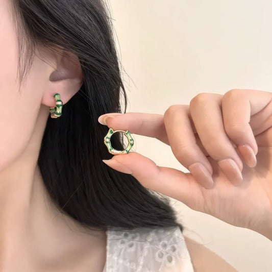  Hand holding a Chinese - style bamboo knot enamel earring, with one earring worn, emphasizing the intricate bamboo - knot design.