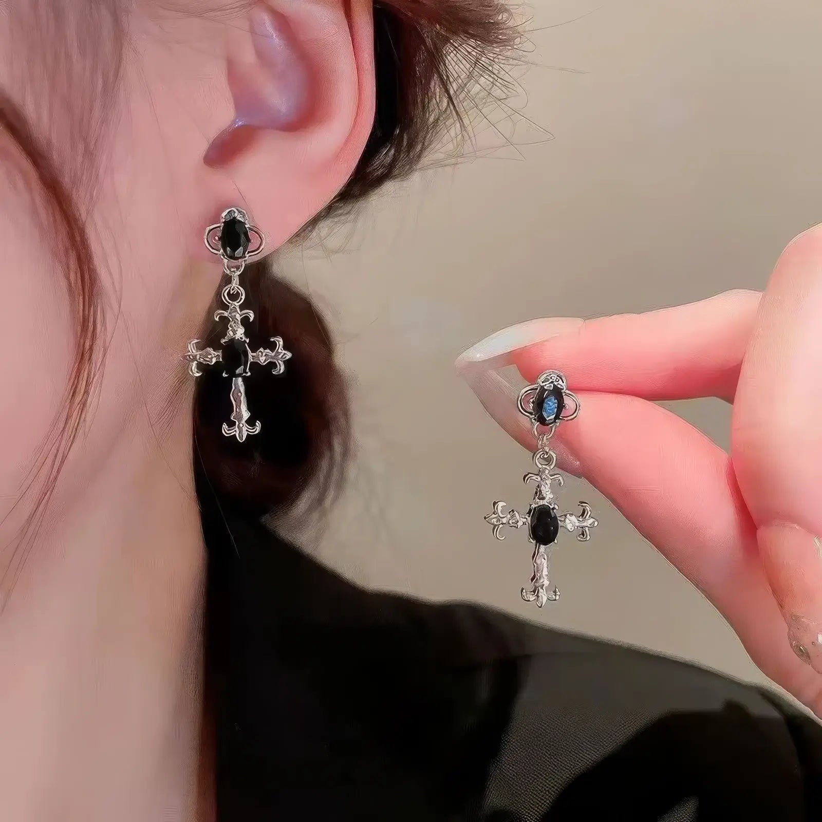 Dark gem cross earring worn on ear, with hand holding the other earring