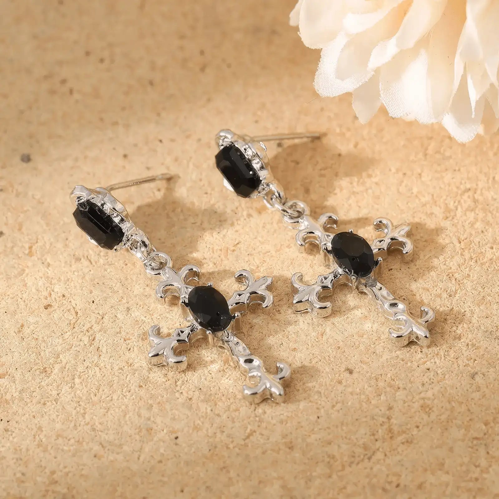 Dark gem cross earrings displayed on a textured surface with a flower