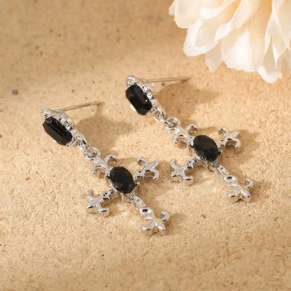 Dark gem cross earrings displayed on a textured surface with a flower