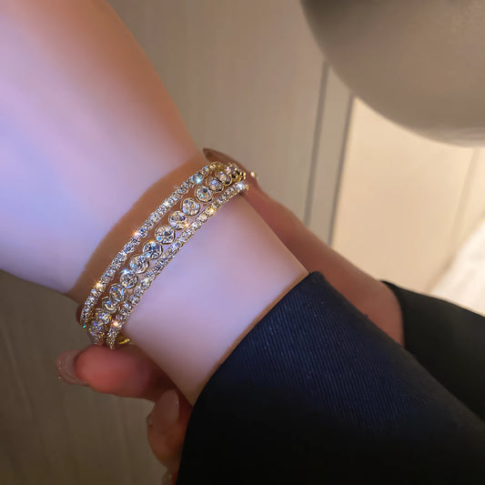 Diamond - inlaid open bracelet worn on wrist, with a dark - colored sleeve.