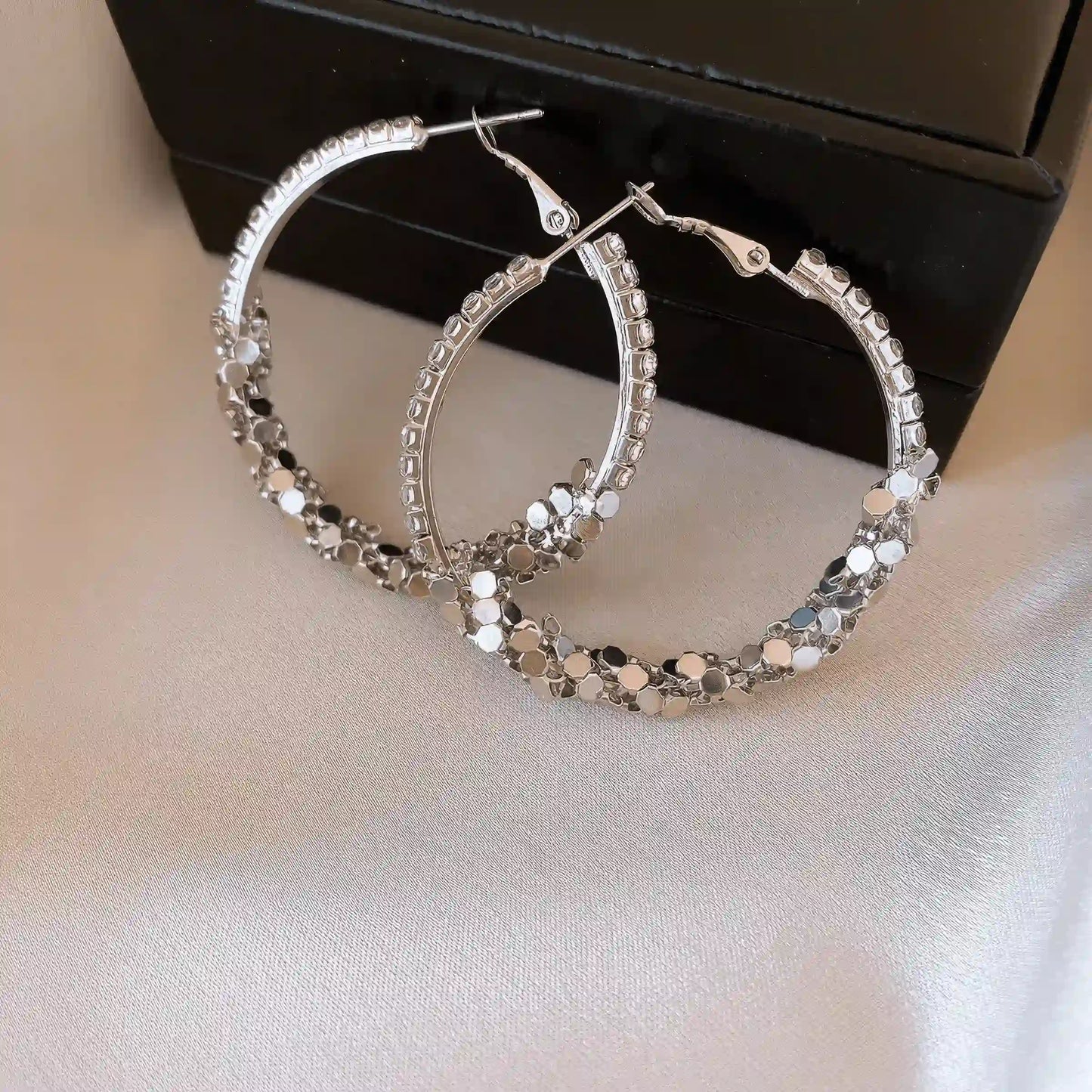 Pair of diamond - inlaid round hoop earrings, displayed on a black box with silver fabric, showcasing the sparkling stone - encrusted design