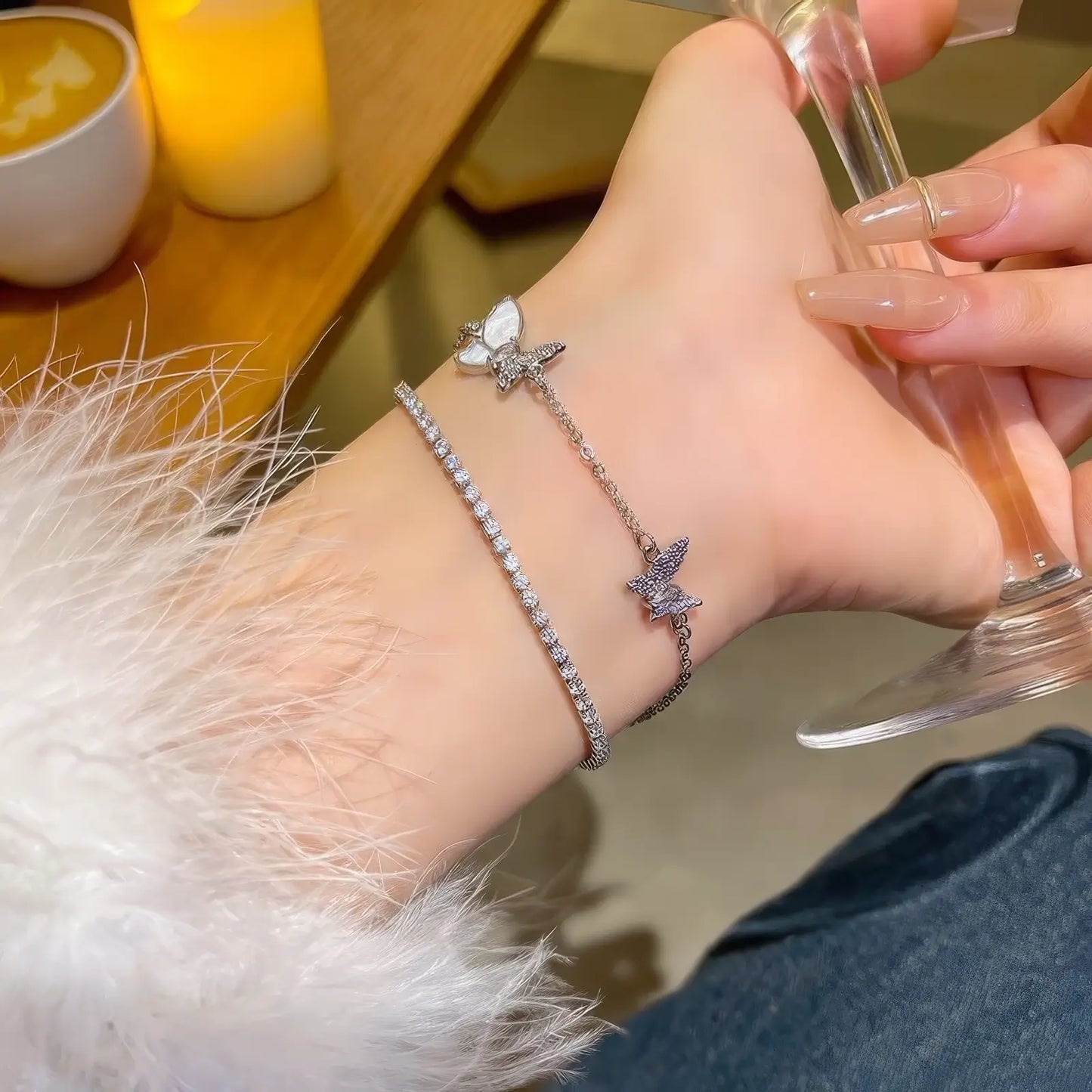 Double - layer butterfly bracelet worn on wrist, with hand holding a glass.
