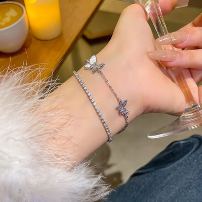 Double - layer butterfly bracelet worn on wrist, with hand holding a glass.