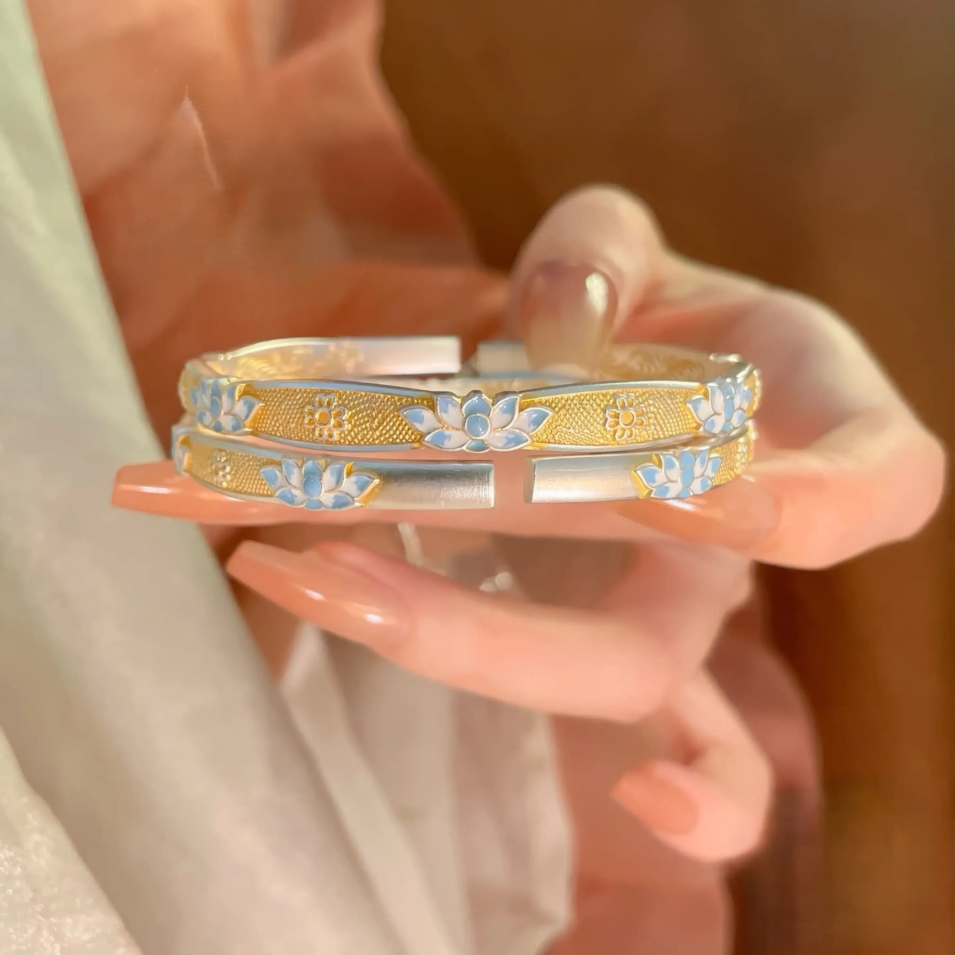 Pair of enamel blue lotus bracelets held in hand, showcasing the blue and gold design.