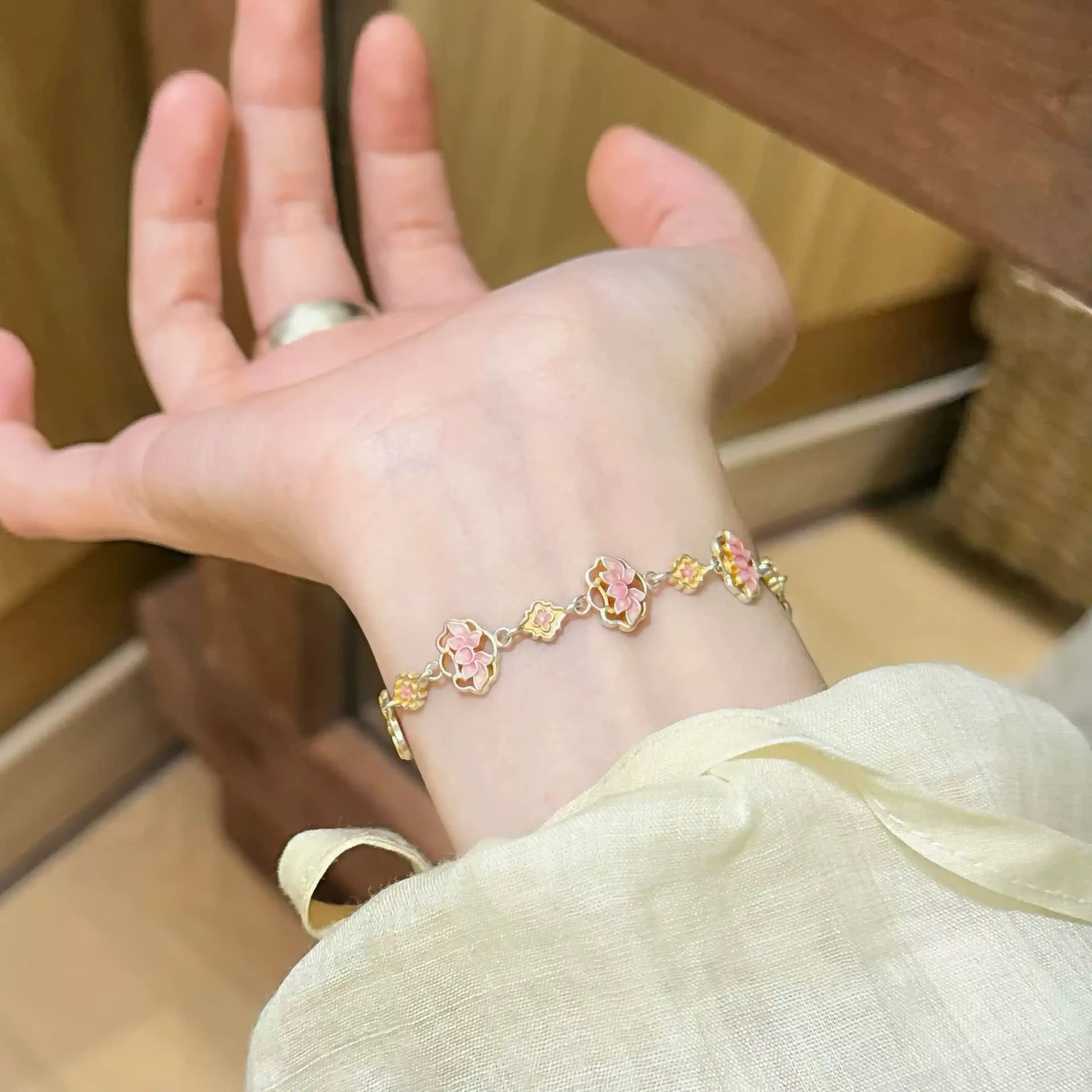 Enamel lotus bracelet worn on wrist, with hand gesture.