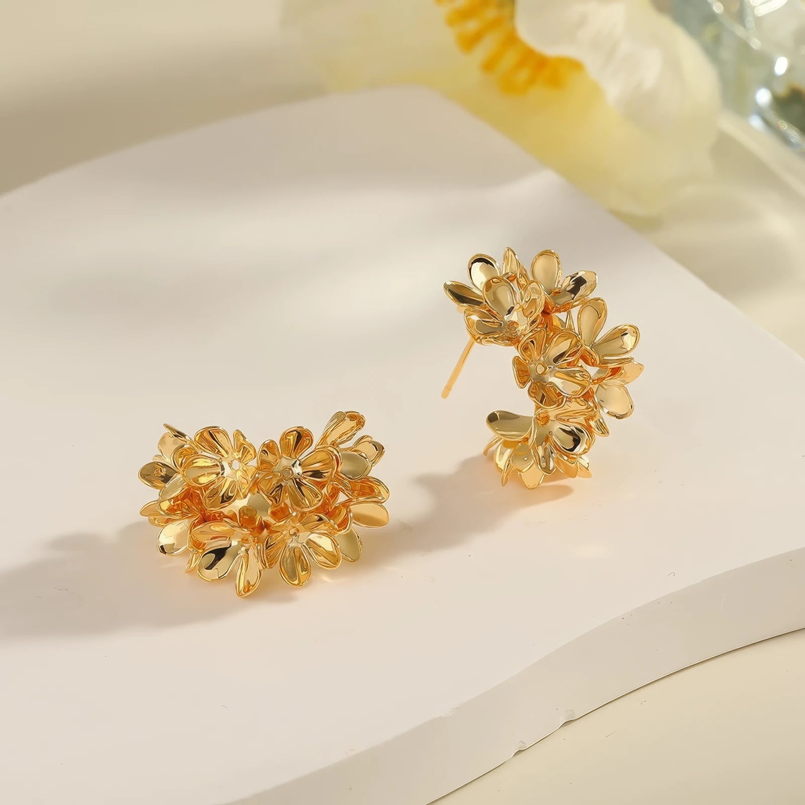 Pair of gold floral curved earrings, displayed on white surface, emphasizing the detailed, flower - clustered design