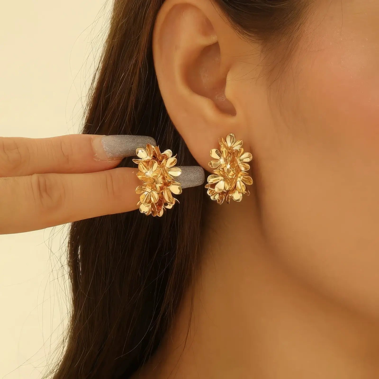 Gold floral curved earrings worn, with hand adjusting, emphasizing the elegant, flower - clustered look