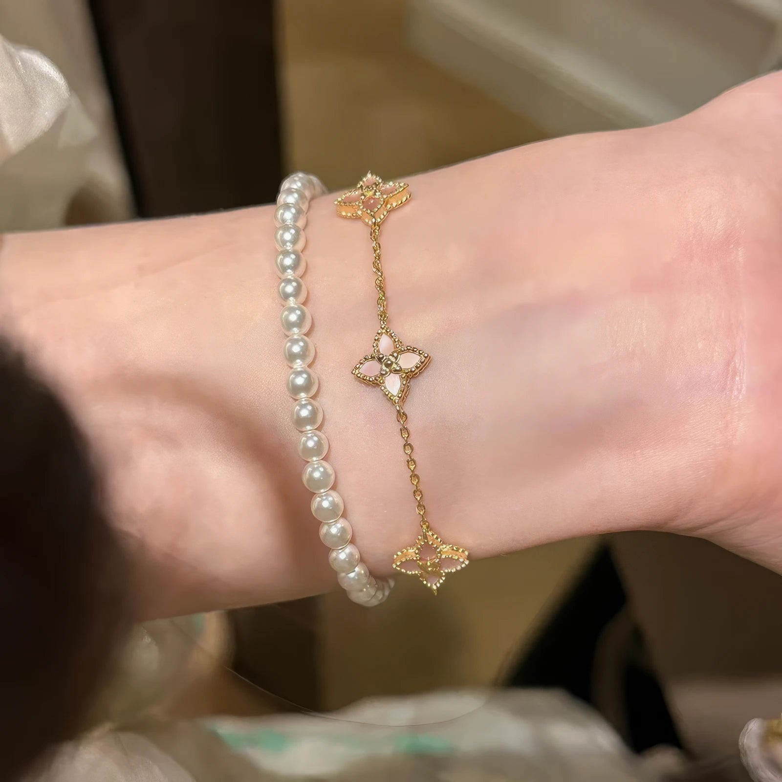 Flower petal pendant bracelet stacked with pearl bracelet on wrist.