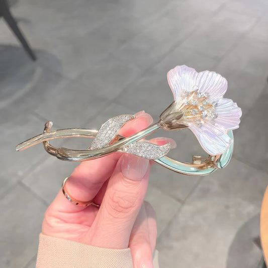 Hand holding ginkgo leaf twist clip with light purple flower, gray background