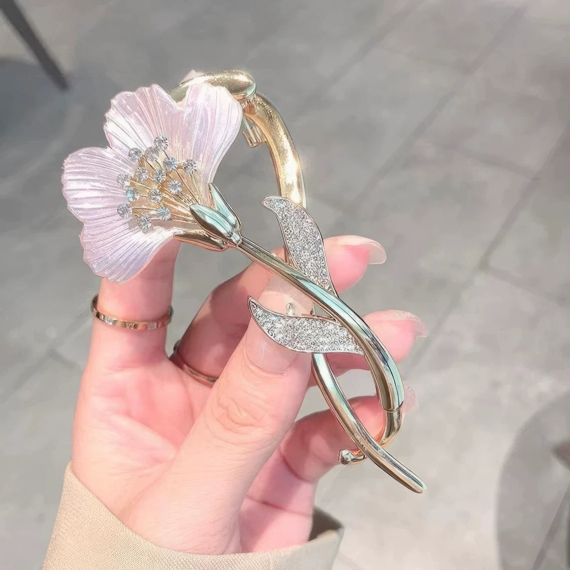 Another view of hand holding ginkgo leaf twist clip with light purple flower, gray background