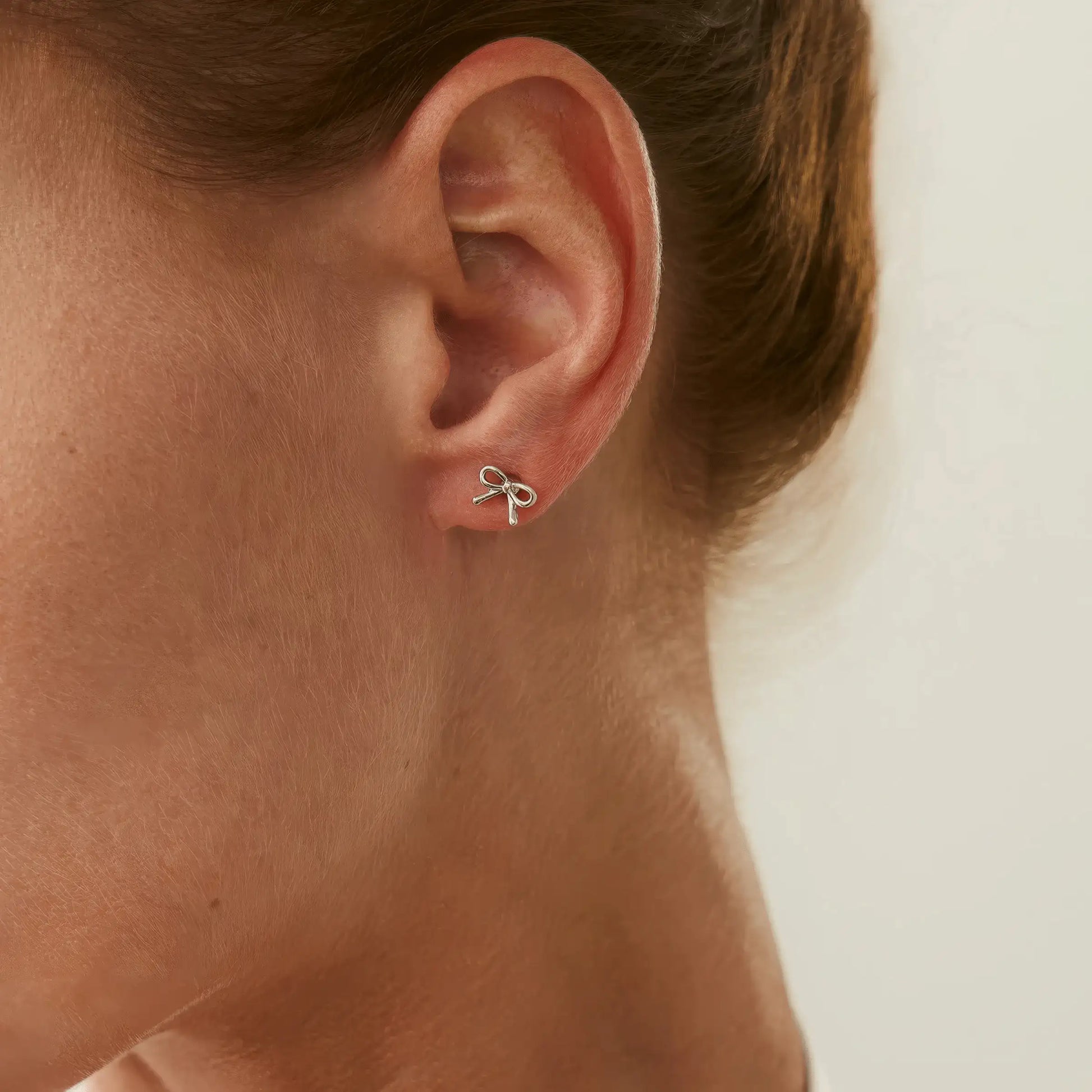 Gold bow tie stud earring worn on ear, showcasing simple and elegant look.